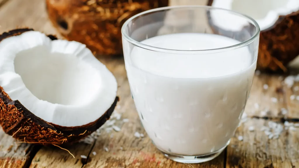 Photograph of cracked open coconut with a glass of coconut milk